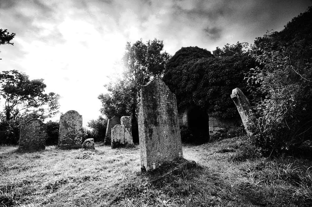Atmospheric black and white image of a graveyard and ruined, ivy covered church.