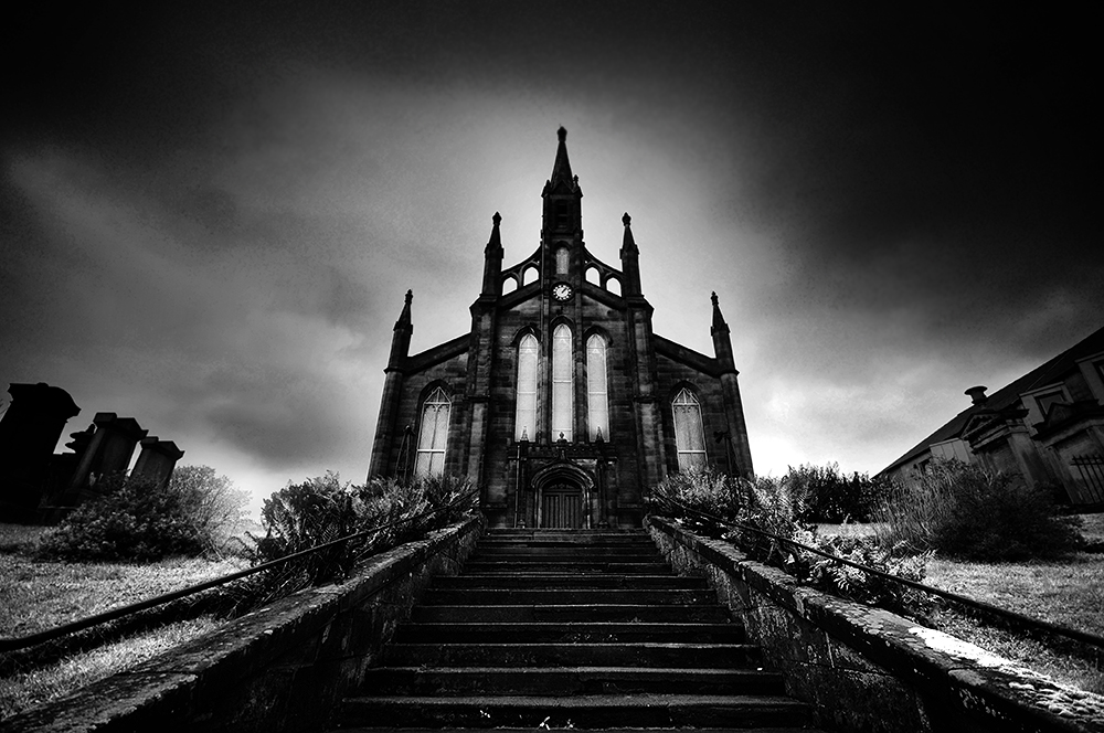 Black and white photo of a gothic church at the top of steep steps, with dark skies above.